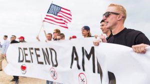 RAM members Daley, nearest at right, Tyler Laube, holding an American flag, and Robert Rundo, far left, display a “Defend America” banner at a pro-Trump rally on March 25, 2017, in Huntington Beach, California.