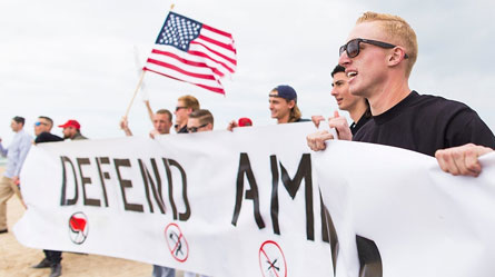 RAM members Daley, nearest at right, Tyler Laube, holding an American flag, and Robert Rundo, far left, display a “Defend America” banner at a pro-Trump rally on March 25, 2017, in Huntington Beach, California.