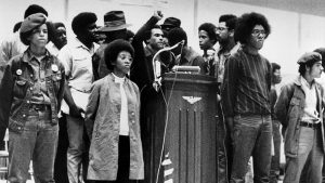 Huey P. Newton, national defense minister of the Black Panther Party, raises his clenched fist behind the podium as he speaks at a convention sponsored by the Black Panthers at Temple University’s McGonigle Hall in Philadelphia, Pa., Saturday, Sept. 5, 1970. He is surrounded by security guards of the movement. The audience gathered is estimated at 6,000 with another thousand outside the crowded hall.