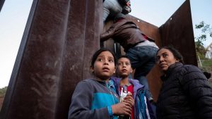 Central American migrants hesitate as others climb the Mexico-US border fence in an attempt to cross to San Diego county, in Playas de Tijuana, Baja California state, Mexico.