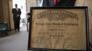 Dexter Vaughn holds his father's embalming certification that hangs above his desk at the Cox Brothers Funeral Home. Image by Evey Wilson