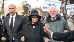 Sens. Cory Booker and Bernie Sanders, seen at a South Carolina NAACP march in January, are two of the 2020 Democratic presidential candidates pressed on the issue of reparations this week.,