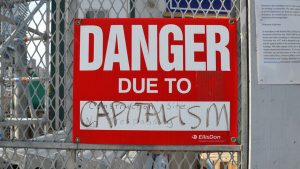 A sign posted on a construction site says, "Danger Due to Capitalism."