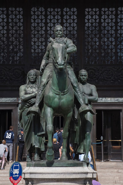 The statue depicts Roosevelt on horseback, with a Native American man and an African man on foot on each side.