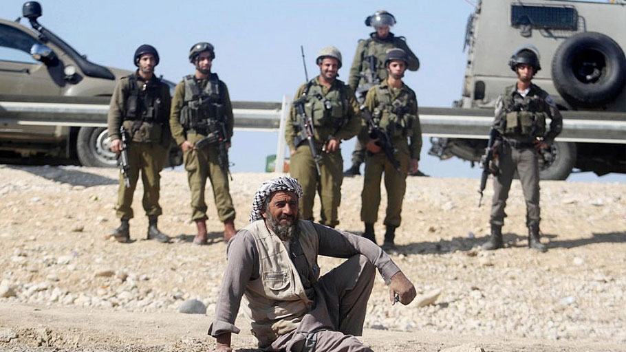 A Palestinian man rests by Israeli soldiers near the site of the old village known as Ein Hijleh, in the Jordan Valley near the West Bank city of Jericho, February 5, 2014.