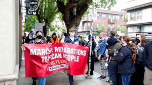 “The march moves past a line of people waiting to enter a shop on Mississippi Avenue in the historically Black Albina neighborhood, which has been gentrified over the past two decades.”