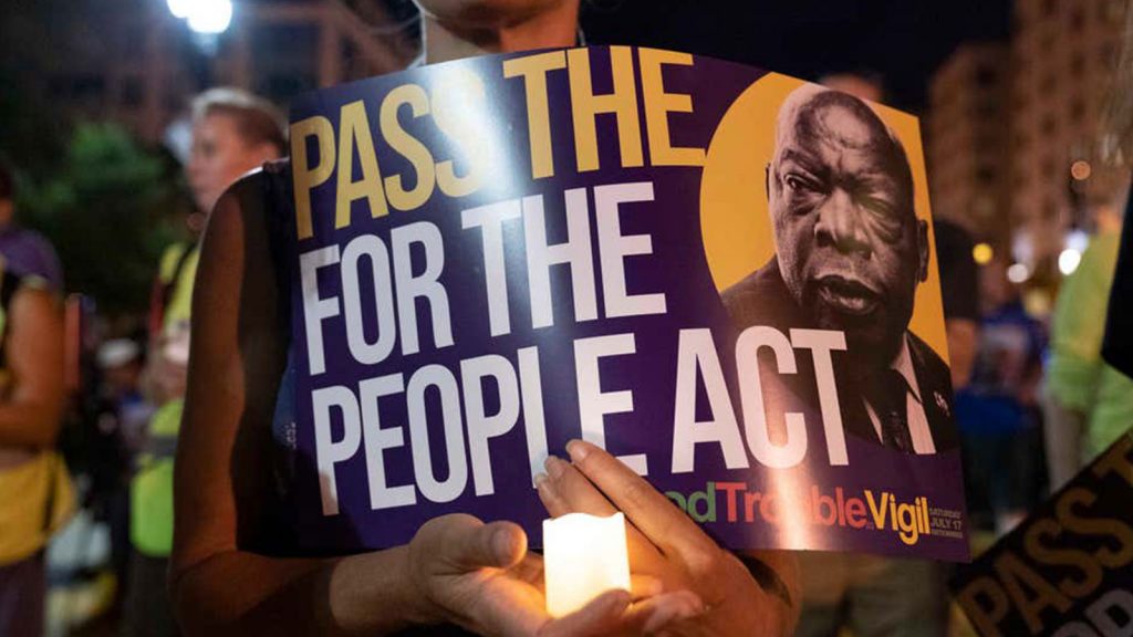 In this July 17, 2021 photo, a person holds a candle and a poster with an image of the late Rep. John Lewis during a rally in support of voting rights, at Black Lives Matter Plaza in Washington.