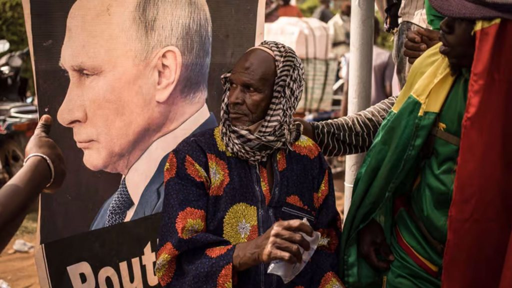 An man sits in front of a portrait of Russian President Vladimir Putin during a demonstration to celebrate France's announcement to withdraw French troops from Mali, in Bamako, on February 19, 2022.