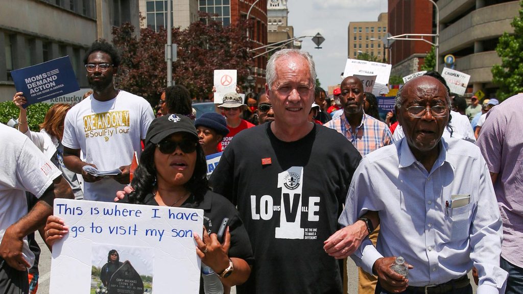 Mayor Greg Fischer locks arms with Rose Smith and Reverend Charles Elliott during a march protesting gun violence in downtown Louisville, Kentucky on June 11, 2022.