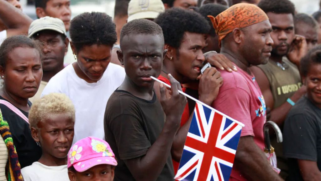 A well-wisher with a Union flag waits the arrival of Britain’s Duke and Duchess of Cambridge in central Honiara, Solomon Islands, Monday, Sept. 17, 2012. Many see Queen Elizabeth II as an anchor to an imperial past whose damage still lingers.