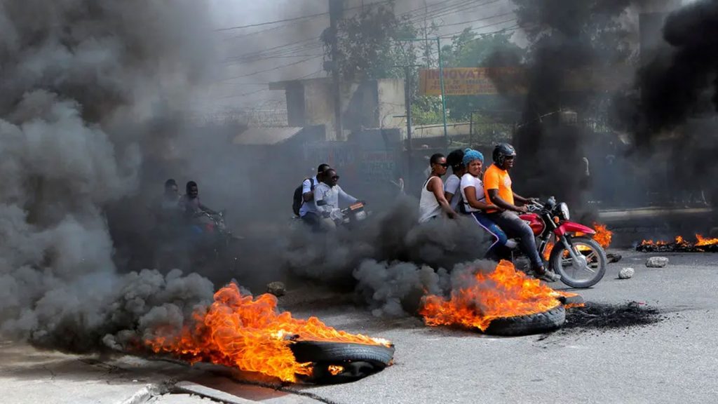 Motorcycle drivers passing through a burning roadblock as anger mounted over fuel shortages that have intensified as a result of gang violence this month in Port-au-Prince.