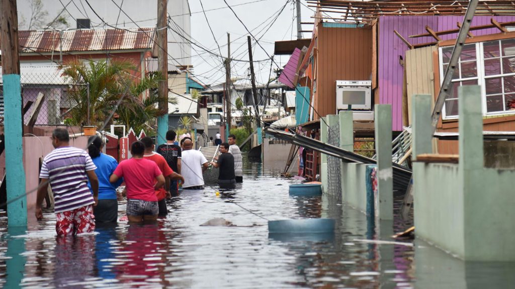 People walk in a flooded street next to damaged houses in Catano town, in Juana Matos, Puerto Rico.