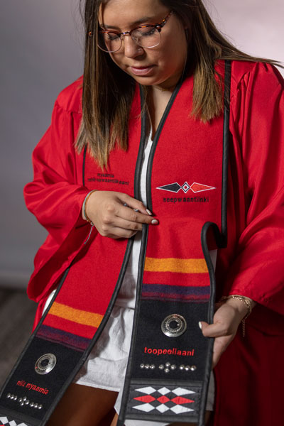 Jenna Corral, a Myaamia Heritage Program participant who graduated from Miami University in 2021, admires her graduation stole featuring traditional ribbonwork and writing in the Myaamia language.