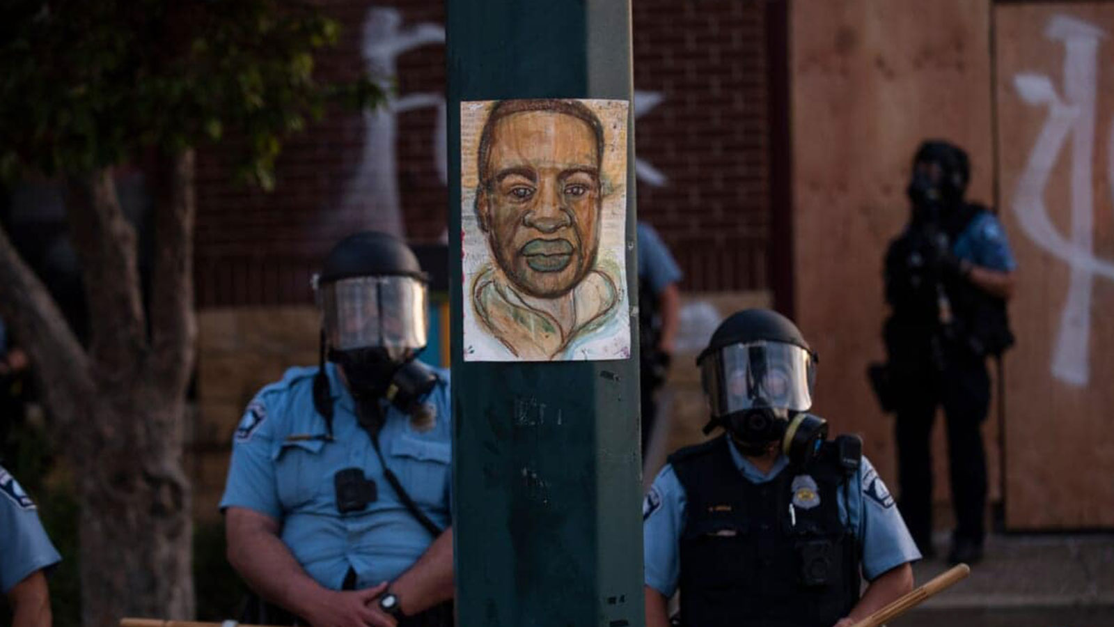 A portrait of George Floyd hangs on a street light pole on May 27, 2020 as police officers stand guard at the Third Police Precinct during a face off with a group of protesters in Minneapolis, Minnesota. 