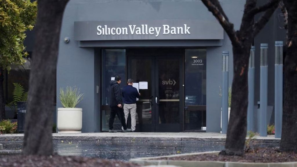A man puts a sign on the door of the Silicon Valley Bank as an onlooker watches at the bank’s headquarters in Santa Clara, California, U.S. March 10, 2023.