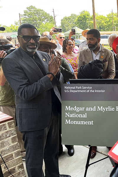 Myrlie Evers holds aloft the ribbon after cutting it to launch their home as a national monument. At her left is her daughter Reena. Mayor Chokwe Antar Lumumba is at the back of the sign. Credit: Herb Boyd photo