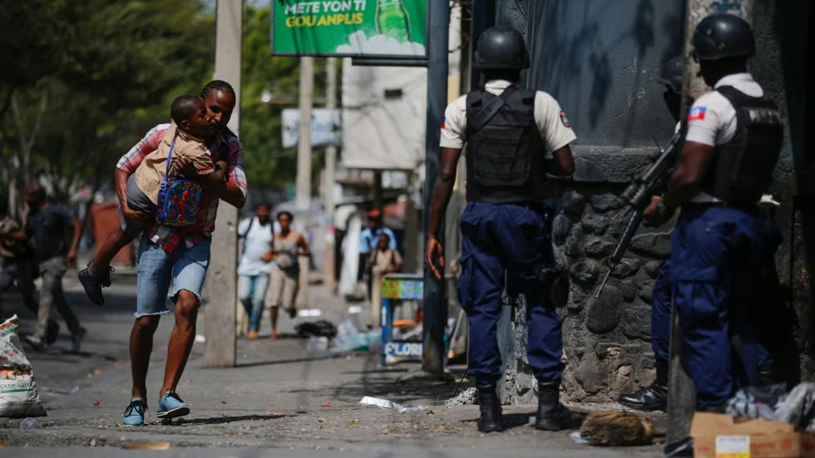A parent, carrying his child after picking him up from school, runs past police as they carry out an operation against gangs in the Bel-Air area of Port-au-Prince on March 3, 2023.