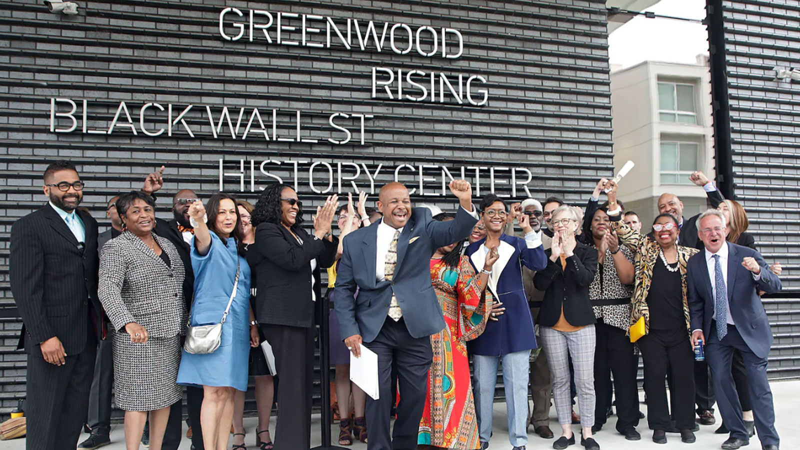 Members of the 1921 Tulsa Race Massacre Centennial Commission, with State Sen. Kevin Matthews in front, cheer in front of the Greenwood Rising Black Wall St. History Center before a dedication in June 2021 in Tulsa.