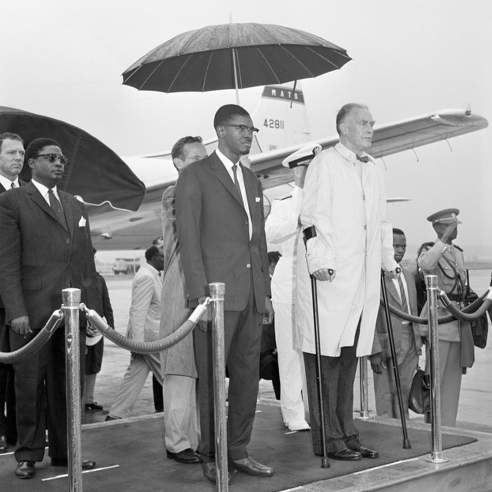 Lumumba, left, of the Republic of the Congo and U.S. Secretary of State Christian Herter stand under an umbrella in the rain during ceremonies at the National Airport in Arlington, Va., July 27, 1960. 