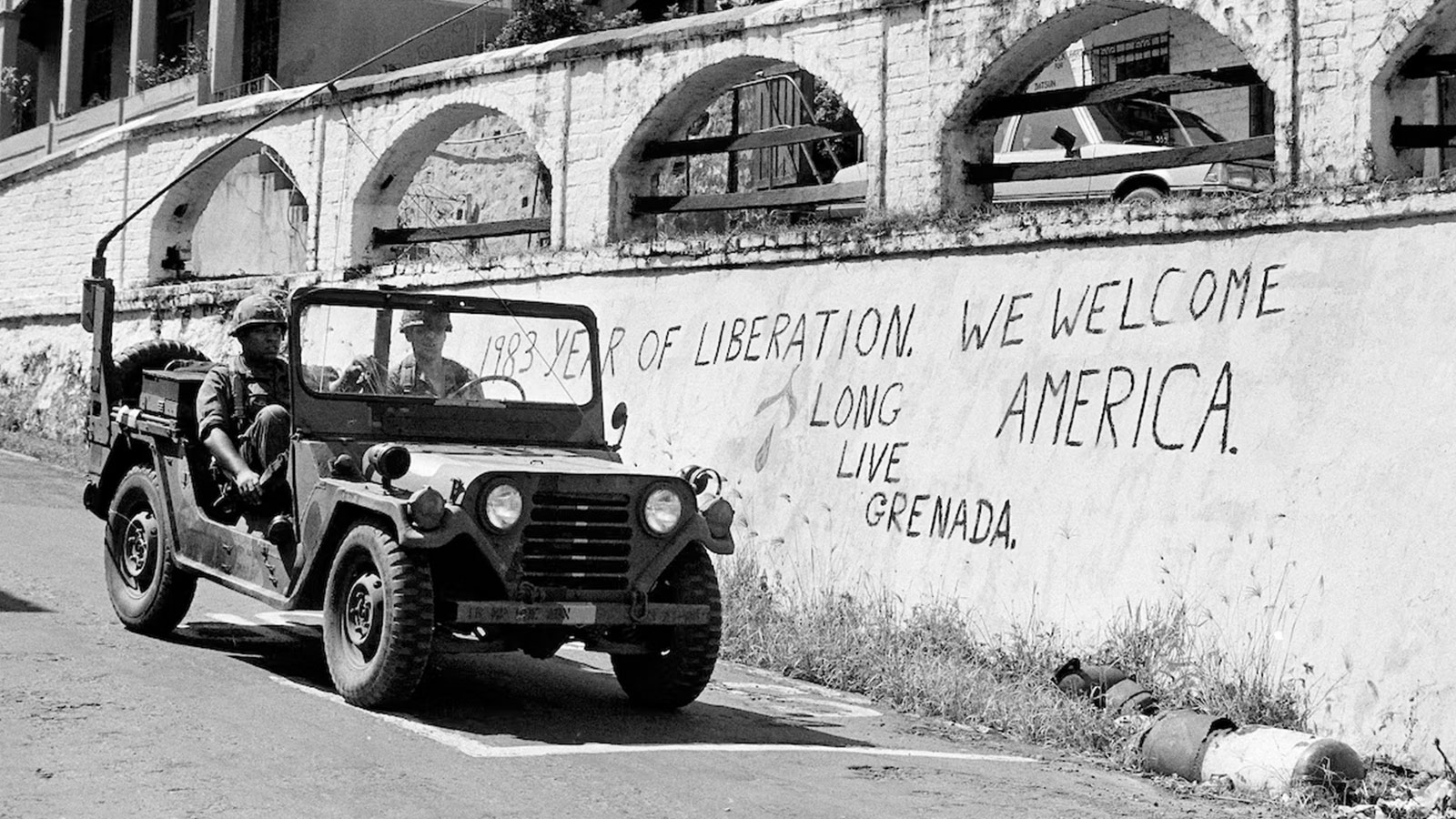 U.S. members of the multinational peacekeeping force drive their jeep past a wall with graffiti welcoming Americans in St. George's, Grenada, Nov. 10, 1983. 