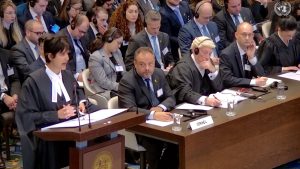 Adila Hassim, attorney for South Africa, addressing the World Court, with the Israel delegation looking on. (UN TV screenshot)