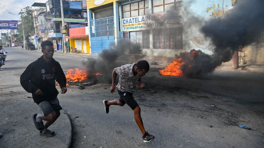 People run past burning tyres during a demonstration calling for the departure of Haitian Prime Minister Ariel Henry in Port-au-Prince on February 6, 2024