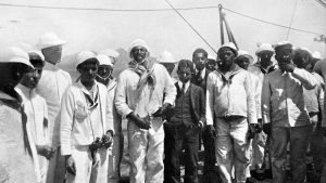 João Cândido Felisberto, centre at left of man in suit, stands among other sailors on the deck of a Brazilian warship in 1910.