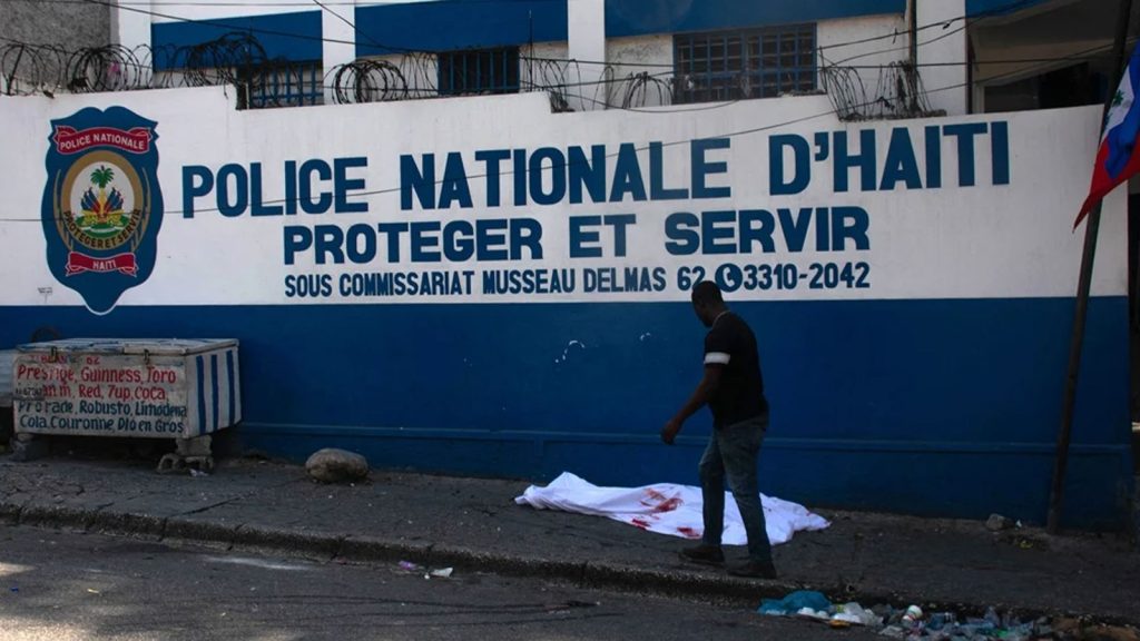 A man walks past the body of a police officer killed amid ongoing gang violence in Port-au-Prince, Haiti, on 20 March 2024. Negotiations to form a transitional council to govern Haiti advanced on 20 March, as the United States airlifted more citizens to safety from gang violence that has plunged the impoverished country into chaos.