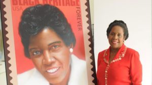 Congresswoman Sheila Jackson Lee standing next to Barbara Jordan U.S. postal stamp display (Sheila Jackson Lee, Flickr).