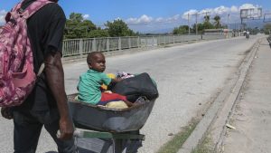 A man pushes a child in a wheelbarrow along a street in Pont-Sonde, Haiti, Monday, Oct. 7, 2024, days after a gang attacked the town.