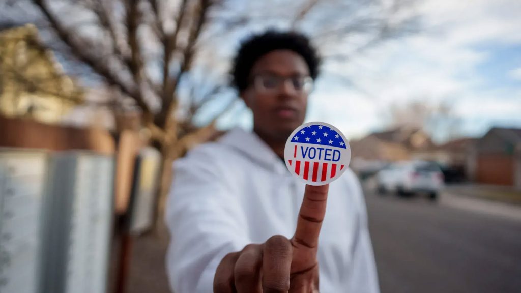 Young Black male holding "voted" sticker