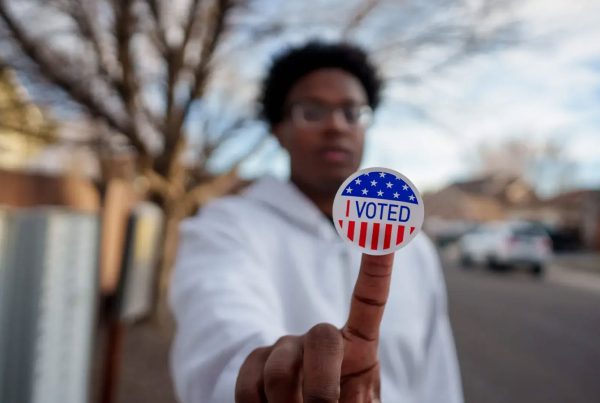 Young Black male holding "voted" sticker