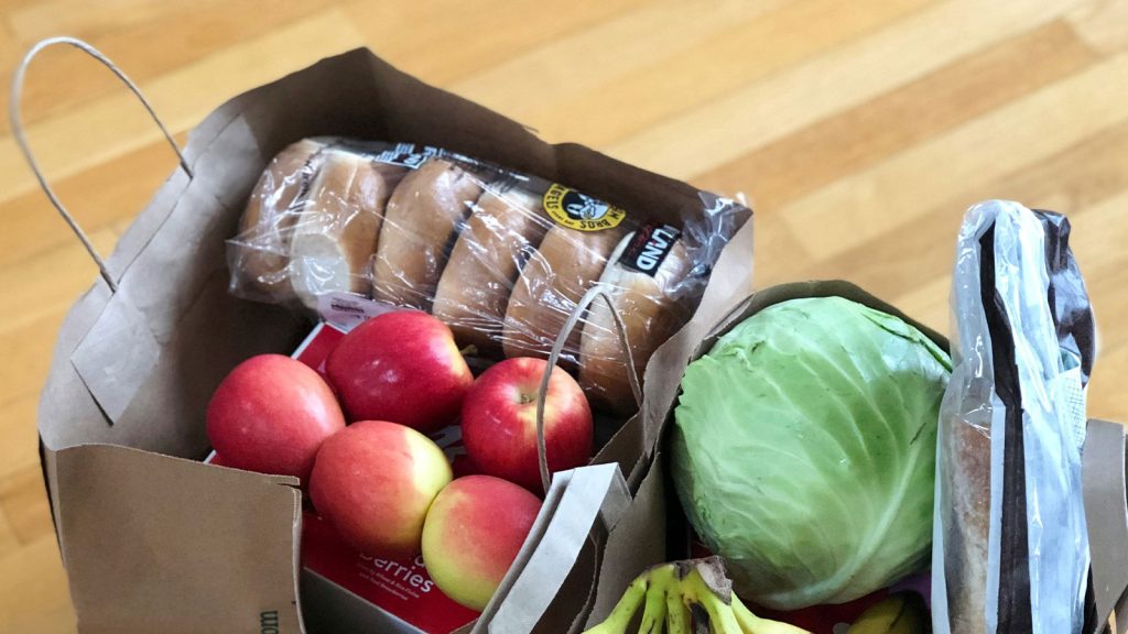 Grocery bags filled with fresh food items on a kitchen floor (Maria Lin Kim, Unsplash)