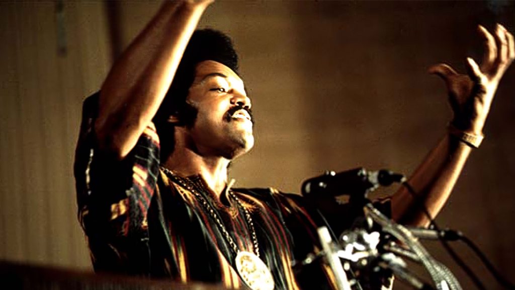 Rev. Jesse Jackson speaking at Operation PUSH headquarters in Chicago, July 1973, raising both hands during a radio broadcast.