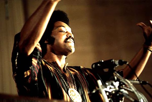 Rev. Jesse Jackson speaking at Operation PUSH headquarters in Chicago, July 1973, raising both hands during a radio broadcast.