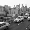 This image captures heavy traffic during sunrise or sunset on the Brooklyn Bridge, with the Manhattan skyline prominently featuring the One World Trade Center in the background.