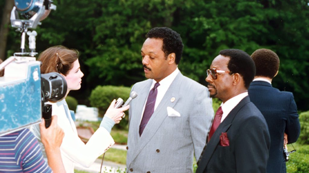 Dr. Ron Daniels and Rev. Jesse Jackson standing together during a televised news interview in the 1980s.