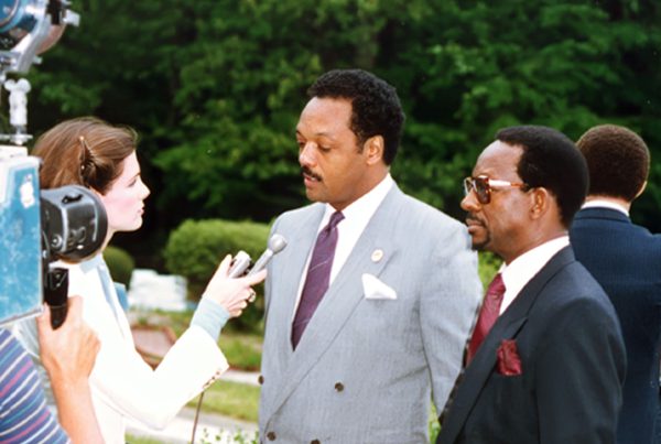 Dr. Ron Daniels and Rev. Jesse Jackson standing together during a televised news interview in the 1980s.