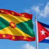 Flags of Grenada and Cuba waving side by side against a blue sky.